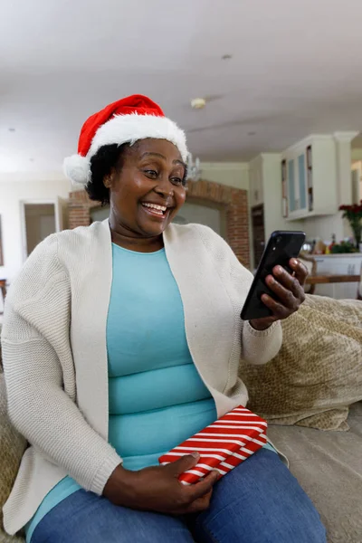 高级非洲裔美国女人 手持智能手机 面带微笑 头戴圣塔帽 优质家庭时间圣诞庆祝活动 — 图库照片