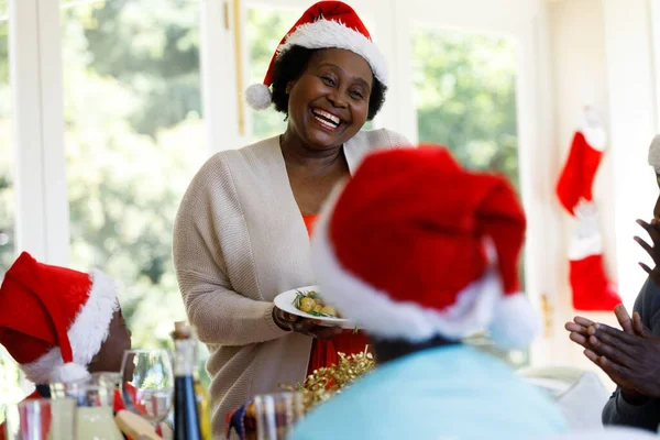 Sênior Afro Americana Servindo Jantar Sorrindo Vestindo Chapéu Papai Noel — Fotografia de Stock