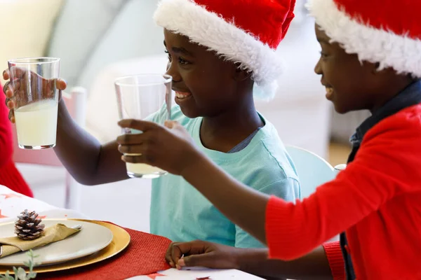 アフリカ系アメリカ人の男の子と女の子のジュースのグラスを保持し 笑顔とサンタの帽子を着用 家族の時間クリスマスのお祝い — ストック写真