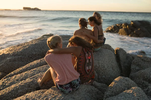 晴れた日にビーチで自由な時間を楽しむ白人女性の友人のグループのサイドビュー 岩の上に座って — ストック写真