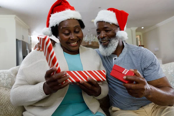 シニアアフリカ系アメリカ人のカップルは 贈り物を開き 笑顔でサンタの帽子をかぶっています 家族の時間クリスマスのお祝い — ストック写真