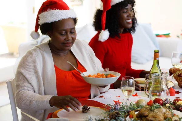 ダイニングルームでの複数世代のアフリカ系アメリカ人の家族は サンタの帽子をかぶって 家族の時間クリスマスのお祝い — ストック写真