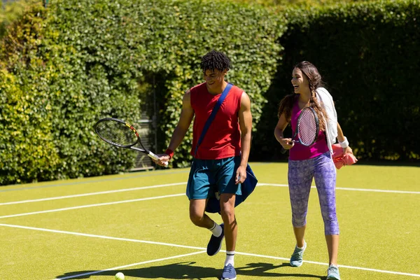 在阳光灿烂的室外网球场上散步的一对快乐而又多姿多彩的情侣 提着袋子和球拍 健康的生活方式 爱好和假期 — 图库照片