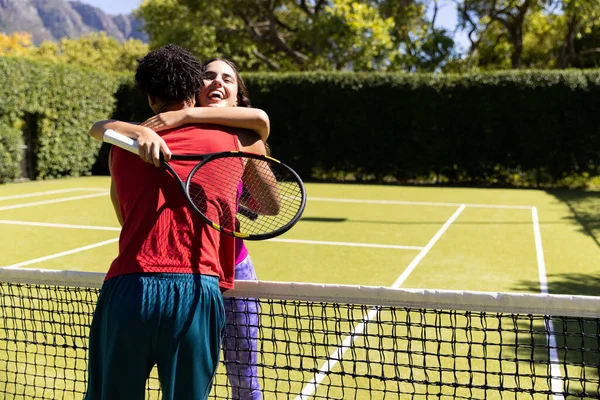 Feliz Pareja Diversa Sosteniendo Raquetas Abrazando Través Red Soleada Cancha — Foto de Stock