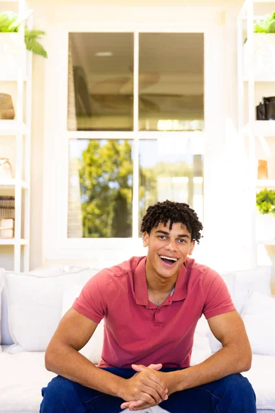 stock image Portrait of happy biracial man sitting on sofa in living room, smiling during video call, copy space. Communication, lifestyle and domestic life.