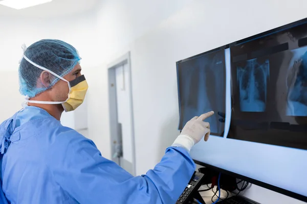 白人男性外科医は手術室のスクリーンでX線を研究している 医療サービス — ストック写真