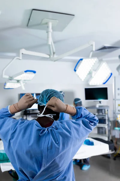 Bakifrån Afrikansk Amerikansk Manlig Kirurg Som Tar Sig Kirurgmask Operationssalen — Stockfoto