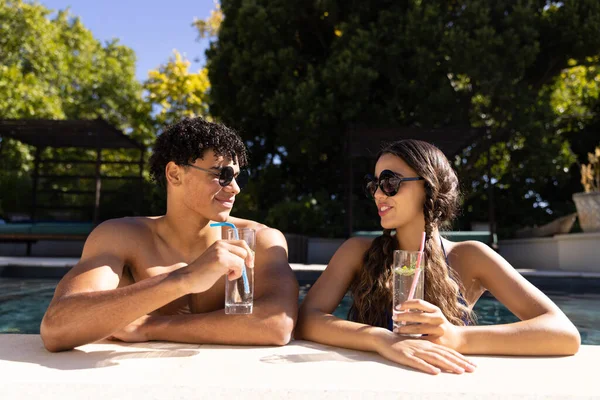 快乐多样的夫妇站在游泳池里 在阳光下与鸡尾酒交谈 业余时间 放松和假期 — 图库照片