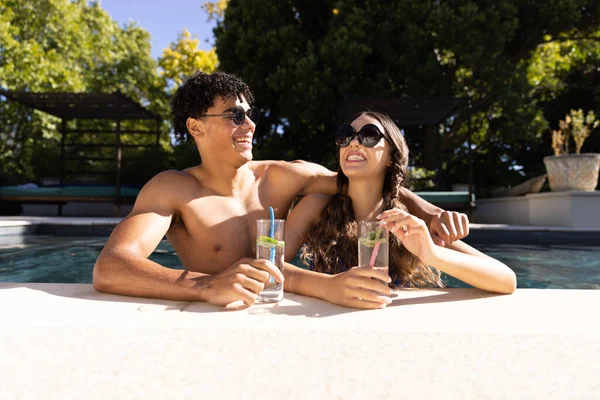 カクテルで太陽の下で笑ってスイミングプールに立って幸せな多様なフィットカップル 自由時間 リラクゼーションと休暇 — ストック写真