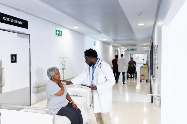 非洲裔美国男性医生 在繁忙的走廊里与各种各样的老年女性病人交谈 医疗和保健服务 — 图库照片