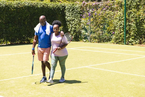 Happy Senior African American Couple Holding Tennis Rackets Walking Sunny — Stock Photo, Image