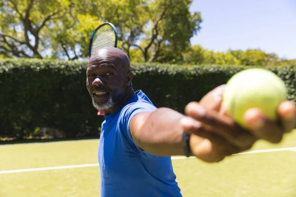 快乐的资深非洲裔美国人打网球 在阳光普照的草地球场上发球 老年生活方式 业余爱好和休闲活动 — 图库照片