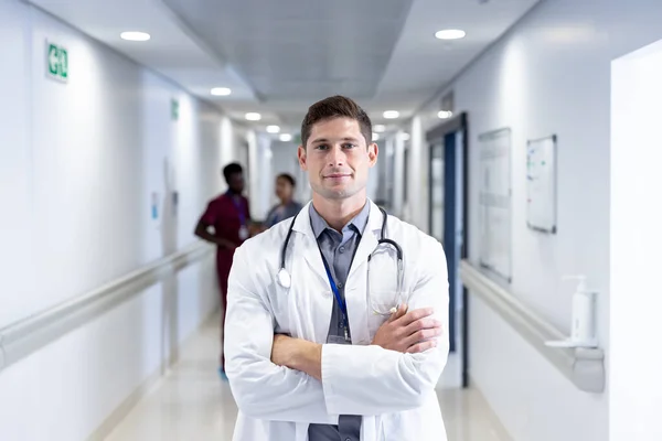 Oförändrat Porträtt Kaukasisk Manlig Läkare Med Armarna Korsade Leende Sjukhuskorridoren — Stockfoto