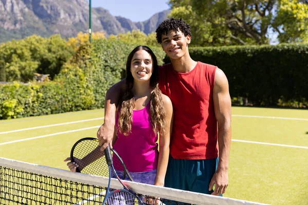 照片上 一对笑容可亲的年轻夫妇拿着网球拍站在法庭上与植物抗衡 不变的 融合的 运动的 竞争的 爱好的 自然和夏天的概念 — 图库照片