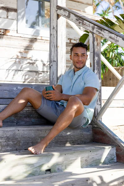 沉思的高加索英俊年轻人拿着咖啡杯 坐在村外的台阶上 未经改动的度假 旅游胜地 生活方式 饮料和娱乐概念 — 图库照片