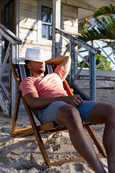 一个戴着帽子的年轻人坐在海滨小屋外面的躺椅上 未经改动的度假 旅游胜地 享受和夏季概念 — 图库照片