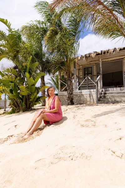 Donna Anziana Caucasica Seduta Sulla Spiaggia Sabbiosa Contro Palme Cottage — Foto Stock