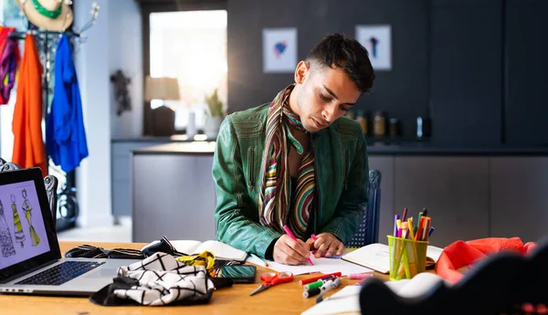 stock image Biracial transgender fashion designer sitting at desk, using laptop and drawing sketches. Gender, fashion, design, communication and lifestyle, unaltered.