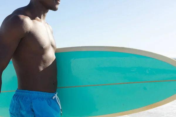 Środkowa Część Afrykańskiego Amerykanina Niosącego Deskę Surfingową Spacerującą Słonecznej Plaży — Zdjęcie stockowe