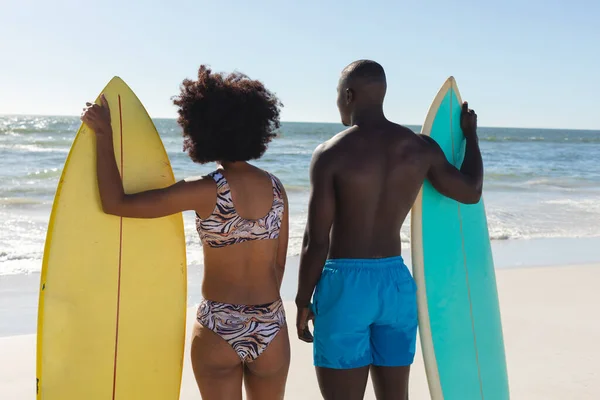 那对健康的非洲裔美国夫妇手持冲浪板站在海边阳光明媚的海滩上的后视镜 健康的生活方式 业余爱好 冲浪和度假 — 图库照片