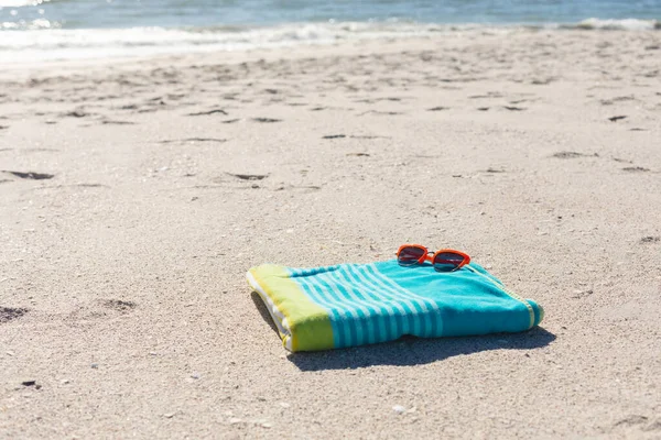 海で日当たりの良い砂のビーチで緑と青の縞模様のタオルに赤いサングラス コピースペース 自由な時間 リラクゼーションとビーチ休暇 — ストック写真