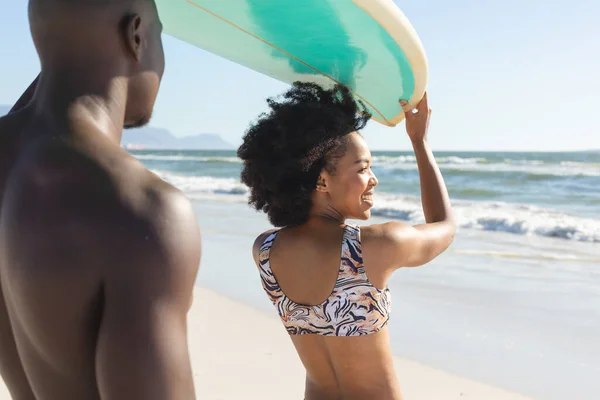 幸せなアフリカ系アメリカ人のカップルの頭の上にサーフボードを保持し 海で日当たりの良いビーチで笑顔 健康的なライフスタイル スポーツ サーフィンや休暇 変更なし — ストック写真