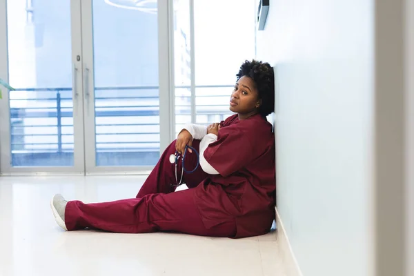 Doctora Afroamericana Cansada Vistiendo Bata Sentada Suelo Pasillo Del Hospital — Foto de Stock