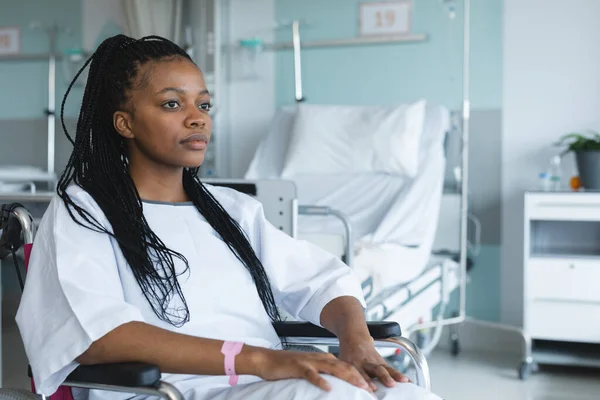 アフリカ系アメリカ人の女性患者は病院のガウンを着て 車椅子で病院の部屋に座っている 変更なし — ストック写真