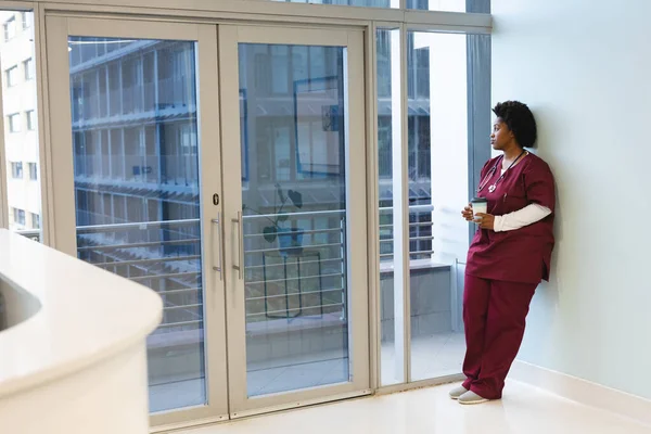 頭の良いアフリカ系アメリカ人の女性医師は スクラブを着用し コーヒーを持ち 窓から見ています 医療と仕事 変更なし — ストック写真