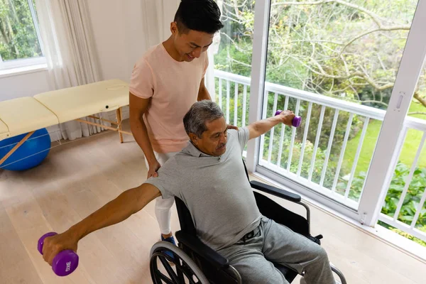 幸せな多様な男性理学療法士のアドバイスやダンベルを使用して車椅子の高齢者 理学療法 高齢者のライフスタイル 変更なし — ストック写真