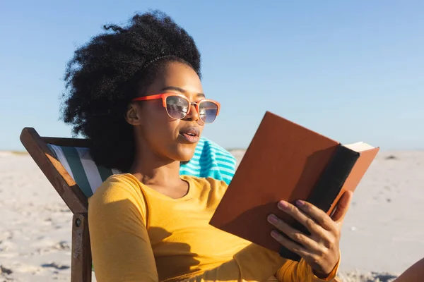 Mujer Afroamericana Feliz Gafas Sol Sentada Tumbona Leyendo Libro Playa —  Fotos de Stock