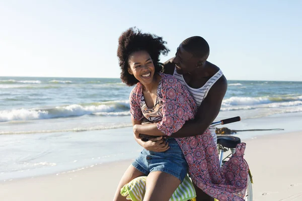 海沿いの日当たりの良いビーチで自転車に乗ることを受け入れる幸せなアフリカ系アメリカ人のカップル ロマンス リラックス 団結と休暇 変更なし — ストック写真