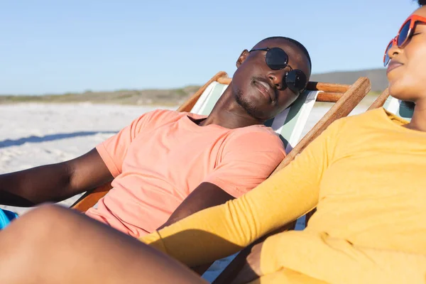Χαρούμενο Ζευγάρι Αφροαμερικανών Που Κάθονται Ξαπλώστρες Χαλαρώνοντας Στην Ηλιόλουστη Παραλία — Φωτογραφία Αρχείου