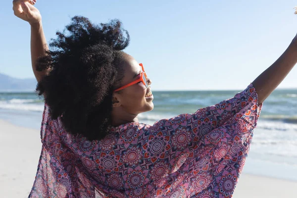 戴着太阳镜的快乐的非洲裔美国女人张开双臂在海上阳光灿烂的海滩上微笑着 放松和假期 — 图库照片