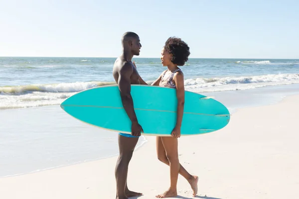 幸せなアフリカ系アメリカ人のカップルは 日当たりの良いビーチに立って互いに笑顔でサーフボードを保持 ロマンス 健康的なライフスタイル スポーツ サーフィンや休暇 変更なし — ストック写真