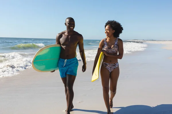 海で日当たりの良いビーチを歩くサーフボードを運ぶアフリカ系アメリカ人のカップルに適しています 健康的なライフスタイル スポーツ サーフィンや休暇 変更なし — ストック写真