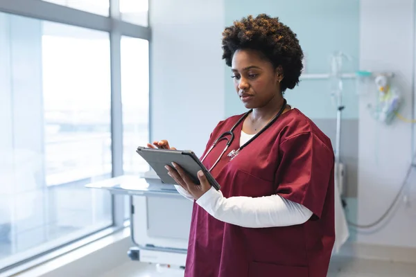 アフリカ系アメリカ人の女性医師は 病院の部屋にタブレットを使用して スクラブと聴診器を身に着けています コミュニケーション 医療と仕事 変更なし — ストック写真