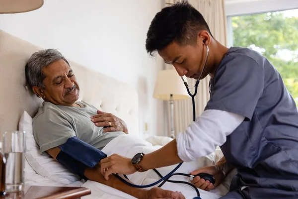 Zróżnicowany Lekarz Przyjmujący Ciśnienie Krwi Starszego Mężczyzny Łóżku Domu Usługi — Zdjęcie stockowe