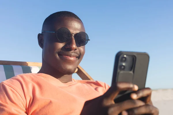 Happy African American Man Sunglasses Sitting Deckchair Using Smartphone Sunny — Stock Photo, Image