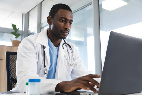 アフリカ系アメリカ人の男性医師は 病院のラップトップを使用して ラボコートと聴診器を身に着けています コミュニケーション 医療と仕事 変更なし — ストック写真