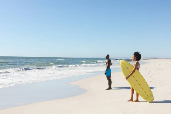 海を探して日当たりの良いビーチに立ってサーフボードとアフリカ系アメリカ人の男性と女性は スペースをコピーします 健康的なライフスタイル スポーツ サーフィンや休暇 変更なし — ストック写真