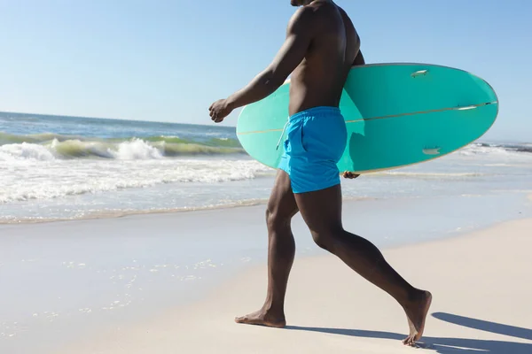 適切なアフリカ系アメリカ人の男性の海に日当たりの良いビーチを歩いてサーフボードを運ぶの低セクションでは スペースをコピーします 健康的なライフスタイル スポーツ サーフィンや休暇 変更なし — ストック写真