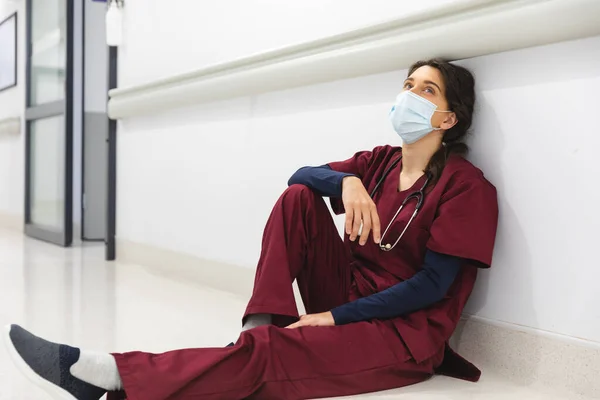 疲惫的高加索女医生 戴着洗涤剂和面罩 坐在医院走廊的地板上 精神健康 保健和工作 — 图库照片