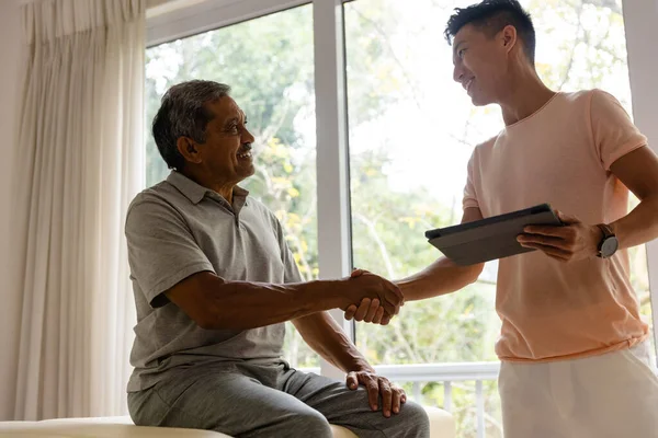 快乐多样的男性理疗师与老年男性患者握手使用平板 物理疗法 交流和老年生活方式 — 图库照片