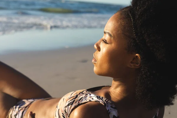 身穿比基尼的富有洞察力的非洲裔美国女人躺在阳光灿烂的海滩上望着大海 闲暇时间和假期 — 图库照片