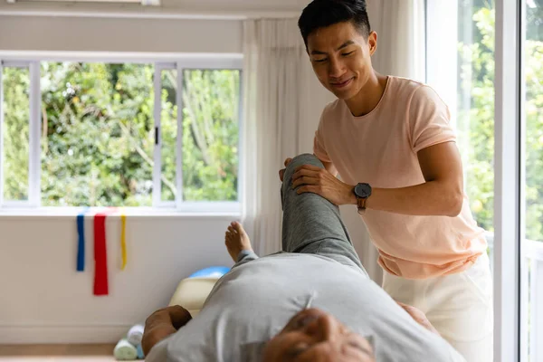 快乐多样的男性理疗师忠告老年男性病人伸展腿 物理疗法 福利和老年生活方式 — 图库照片