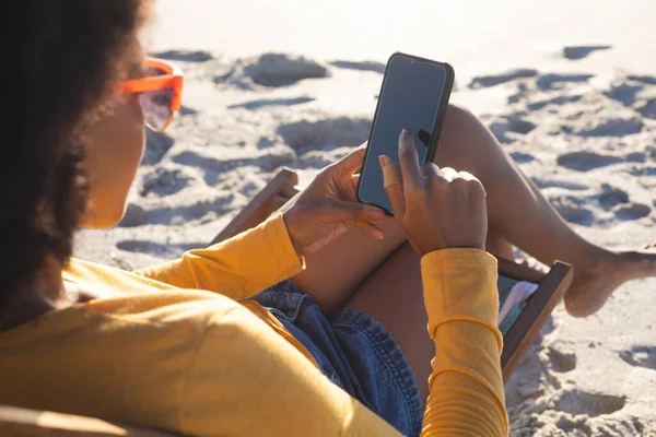 Afroamerikanerin Mit Sonnenbrille Sitzt Liegestuhl Mit Smartphone Sonnigen Strand Sommer — Stockfoto