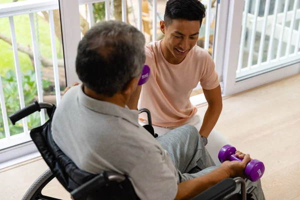 幸せな多様な男性理学療法士のアドバイスやダンベルを使用して車椅子の高齢者 理学療法 高齢者のライフスタイル 変更なし — ストック写真