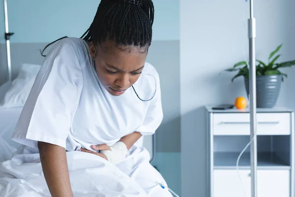 アフリカ系アメリカ人の女性患者がベッドに座り 病院の部屋で胃を保持している 変更なし — ストック写真