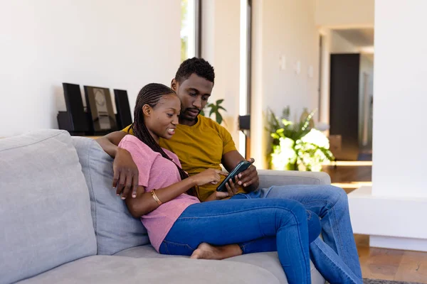 快乐的非洲裔美国夫妇在家里的沙发上微笑 拥抱和使用智能手机 生活方式 爱情和家庭生活 未经调整的 — 图库照片
